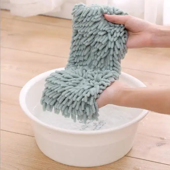 Grey chenille mop pad being rinsed by hand in a white bowl of water