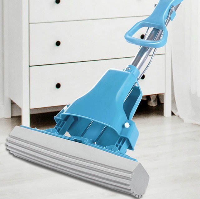 Blue butterfly-fold sponge mop with grey PVA head on a light floor beside a chest of drawers