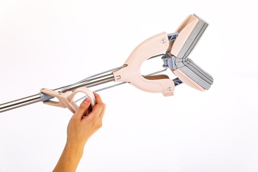 Hand on the pull ring of the pink sponge mop, rods drawing the wings together