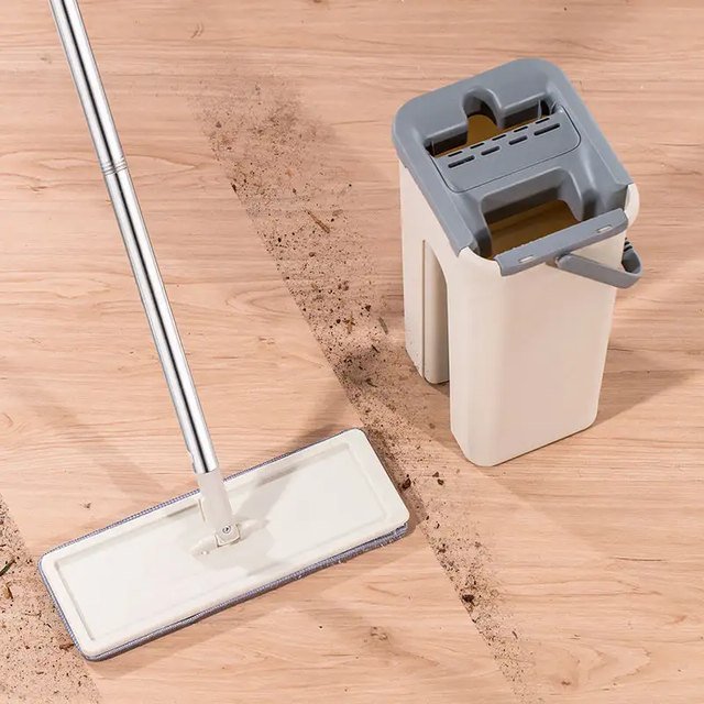 Flat mop beside its beige squeeze bucket on a wooden floor with a dirt trail