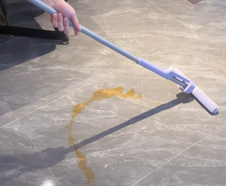Mini sponge mop pushed towards a liquid spill on grey stone tiles