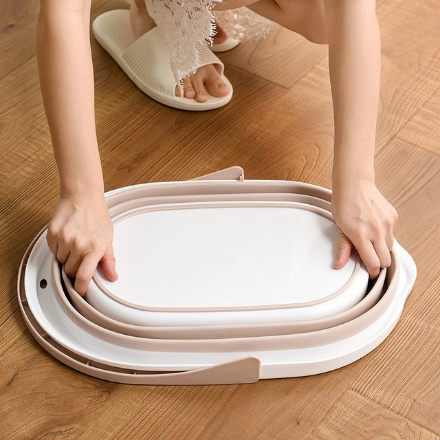 Hands pressing the collapsible oval mop bucket down flat on a wooden floor