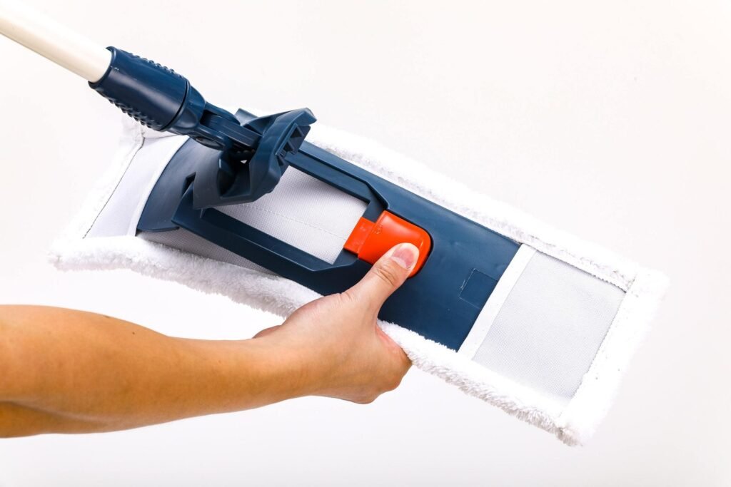 Hand pushing the orange slider on a navy folding flat mop frame to change the pad