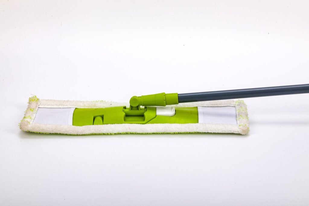 Side view of the green folding flat mop frame on a white microfiber pad